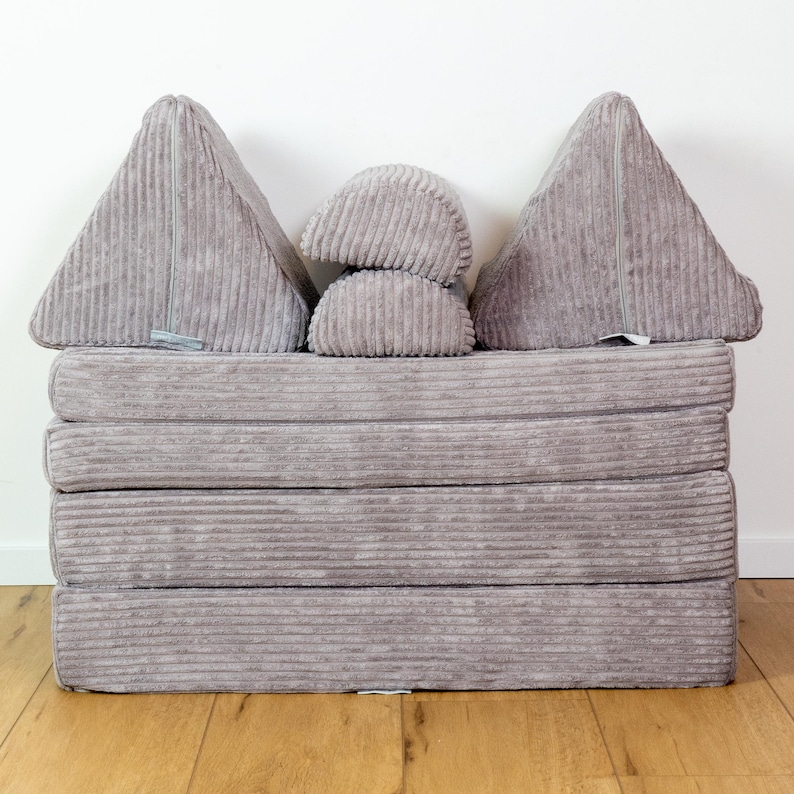 May include: A grey corduroy futon mattress with four foldable sections and two grey corduroy wedge pillows. The futon is folded into a sofa shape.