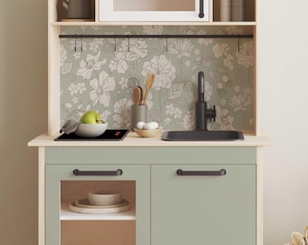 May include: A light green toy kitchen playset with a black sink, stovetop, and cabinet doors. The backsplash features a floral wallpaper design with white flowers on a light green background.