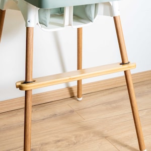 May include: A wooden safety bar for a high chair, with black rubber straps to secure it to the chair legs.