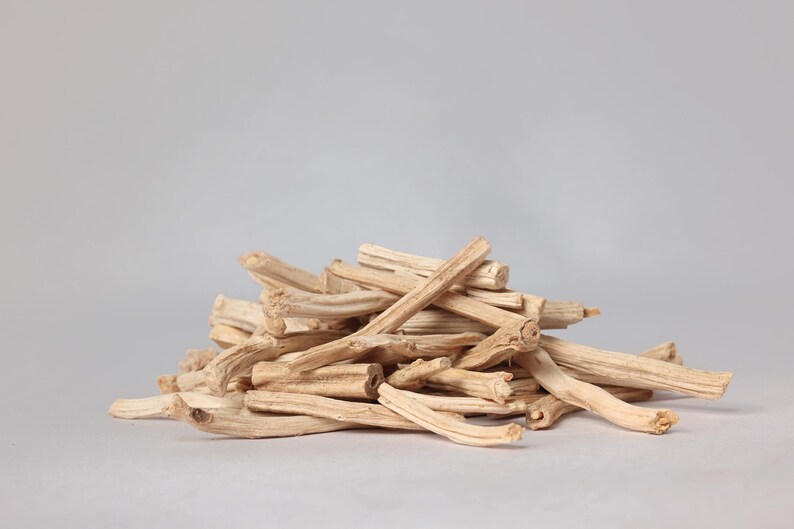 May include: A pile of light beige, dried sticks, possibly incense or kindling, against a plain gray background. The sticks are of varying lengths and thicknesses, with a natural, textured appearance.