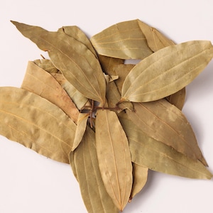 May include: A cluster of dried bay leaves, showcasing a light brown color and textured surfaces. The leaves are arranged in a loose, overlapping pattern against a white background, highlighting their natural form and detail. Ideal for culinary use.