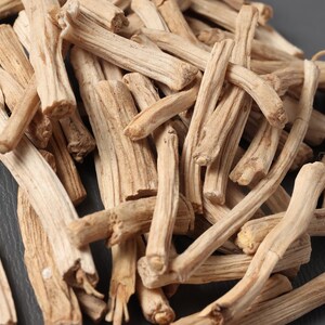 May include: Close-up of a pile of dried, light brown, woody stems. The stems have a rough texture and varying shapes, with some curved and others straight. The background is a dark gray surface.