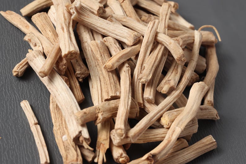 May include: Close-up of a pile of dried, light brown, woody stems. The stems have a rough texture and varying shapes, with some curved and others straight. The background is a dark gray surface.