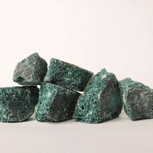 Op de afbeelding: Een verzameling onregelmatig gevormde, donkergroene rotsen met een textuur, poreus oppervlak. De rotsen zijn op elkaar gestapeld, waarbij hun verschillende maten en vormen te zien zijn. De algehele uitstraling is natuurlijk en aards.