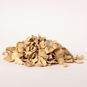 May include: A pile of dried ginger slices, tan in color, against a white background. The ginger pieces are irregularly shaped and appear to be dehydrated. The image is well-lit, highlighting the texture and color of the ginger.