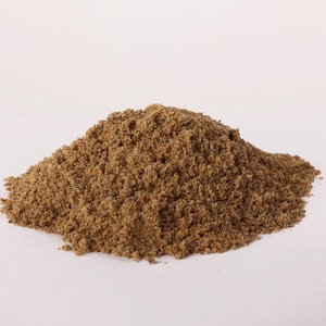 Könnte beinhalten: Ein Haufen feinen, hellbraunen Sandes vor einem weißen Hintergrund. Der Sand wirkt trocken und hat eine leicht raue Textur. Das Bild ist gut beleuchtet und hebt die natürliche Farbe und die granularen Details des Sandes hervor.