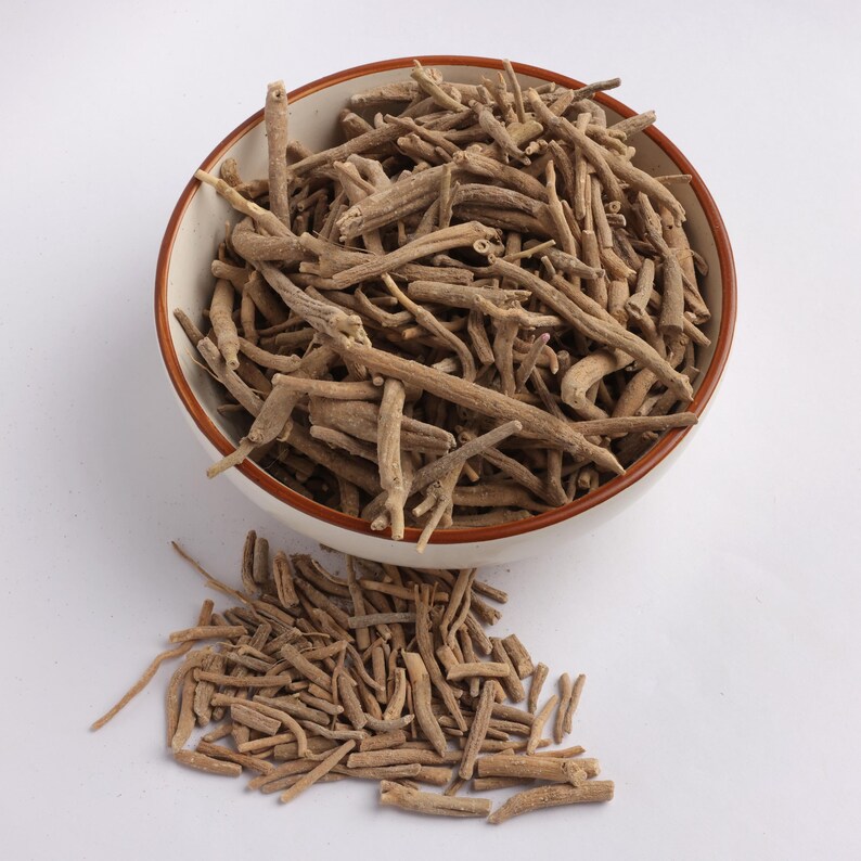 May include: A white bowl with a brown rim filled with dried, light brown, stick-like pieces. Some of the pieces are scattered outside the bowl on a white surface. The contents appear to be a natural product, possibly herbs or roots.