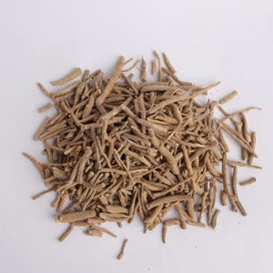 May include: A pile of dried, light brown ashwagandha roots on a white background. The roots are of varying lengths and thicknesses, with a rough, textured appearance. The image is a close-up, showing the details of the herbal product.