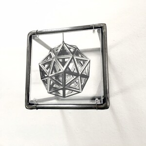May include: A black and white geometric design of a sphere is framed in a silver metal frame with glass.