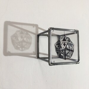 May include: A silver metal cube with a clear glass panel on each side. Inside the cube is a black and white image of a geometric shape.