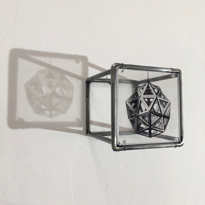May include: A silver metal cube with a clear glass panel on each side. Inside the cube is a black and white image of a geometric shape.