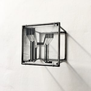 May include: A black and white drawing of a building with columns is framed in a black metal cube. The cube is hanging on a white wall.