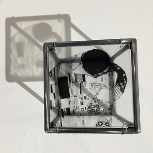 3d metal wall art sculpture with an transparent art print of the Klimt painting The Kiss. The black and white image is reflected like a shadow on the wall.