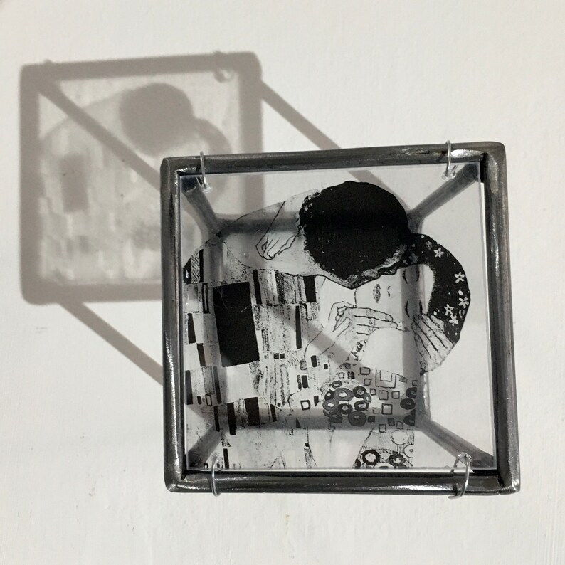 3d metal wall art sculpture with an transparent art print of the Klimt painting The Kiss. The black and white image is reflected like a shadow on the wall.