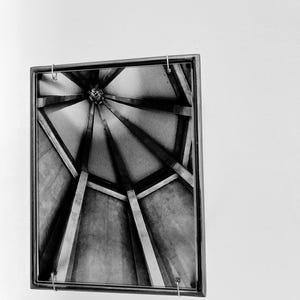Peut inclure: Un cadre noir rectangulaire contenant une photographie en noir et blanc d'une structure architecturale conique. L'image présente des poutres convergentes menant à un point central, créant un motif géométrique avec un contraste élevé.