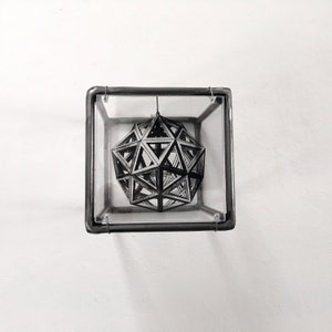 May include: A black and white geometric design of a sphere is suspended inside a clear glass cube with a metal frame.