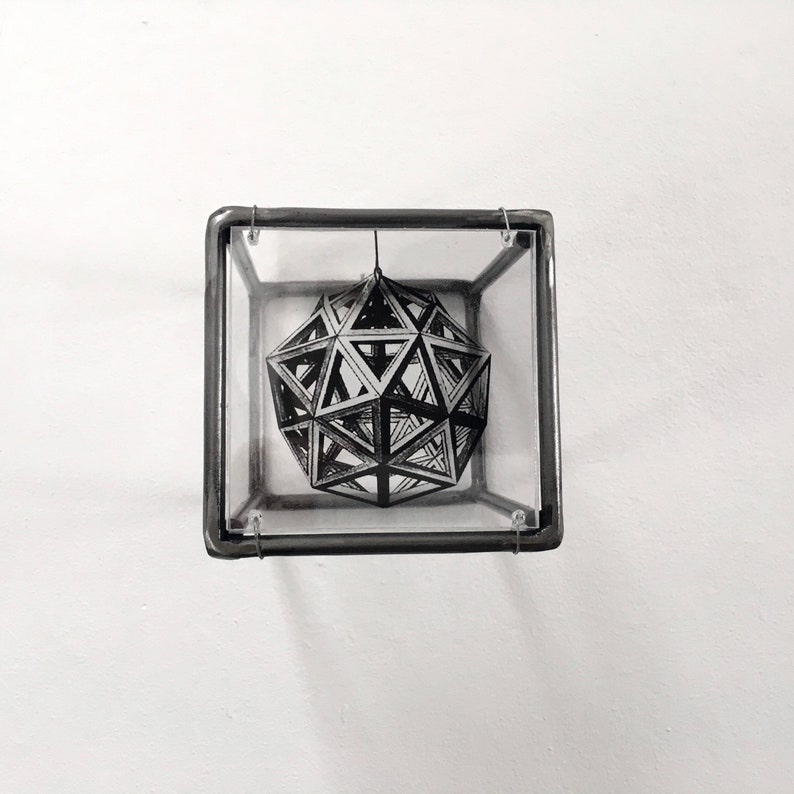 May include: A black and white geometric design of a sphere is suspended inside a clear glass cube with a metal frame.