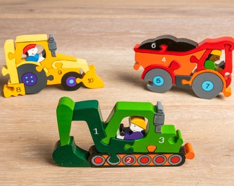 Puede incluir: Tres vehículos de construcción de madera de juguete con piezas de rompecabezas numeradas. Un bulldozer amarillo, un camión volquete rojo y una excavadora verde. Cada vehículo tiene una figura de conductor en el interior.