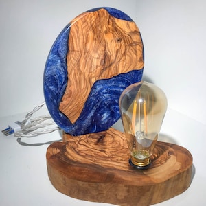 May include: A wooden lamp base with a blue and brown resin inlay and a clear glass light bulb. The base is shaped like a circle and has a natural wood finish.