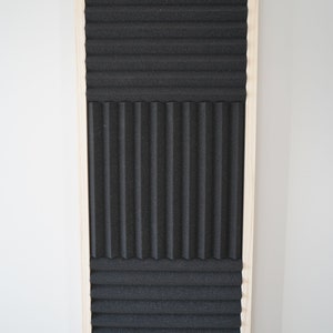 May include: A black acoustic foam panel with a wood frame. The foam is arranged in three sections with different patterns.
