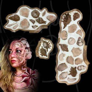 Può includere: Una persona con un complesso trucco a tema polpo sul viso e sul petto, caratterizzato da tentacoli e ventose, accanto a tre stampi in silicone irregolari di colore chiaro contenenti varie forme di conchiglie, inclusi disegni a spirale e a ventaglio.