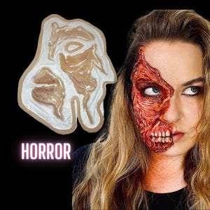 Könnte beinhalten: Eine Silikonform zum Erstellen eines Spezialeffekt-Make-ups. Die Form ist wie ein menschliches Gesicht geformt, bei dem ein Teil des Gesichts fehlt und die darunter liegende Haut und Knochen freilegen. Die Form ist weiß mit einem beigefarbenen Hautton im Inneren. Der Text "HORROR" ist in rosa Buchstaben unter der Form geschrieben.