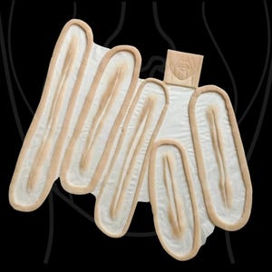 Può includere: Uno stampo in silicone beige caratterizzato da molteplici cavità ovali allungate con bordi rialzati. Lo stampo include una piccola sezione rettangolare nella parte superiore con un grafico in rilievo di una bocca e lingua umana, su sfondo nero.