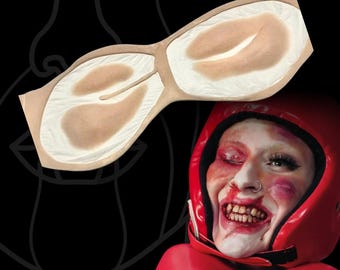May include: A beige prosthetic nose piece with a textured surface and a central bridge, shown alongside a person wearing a red boxing helmet and gloves, with makeup applied to simulate facial bruising, a swollen eye, and stained teeth.