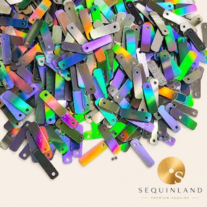 May include: A collection of rectangular, iridescent sequins featuring a holographic finish that shifts between green, purple, and blue tones. Each small, flat piece has a single circular hole at one end. The logo for Sequinland Premium Sequins is visible.