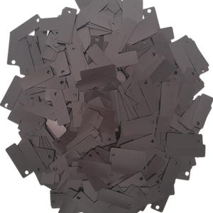 May include: A large pile of dark gray metal tags with holes in the top. The tags are rectangular and have a slightly textured surface.