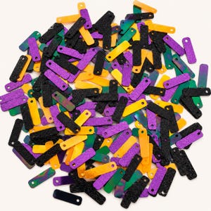 May include: A collection of small, rectangular, flat plastic pieces in black, purple, orange, and green. Each piece features a single circular hole at one end. The black pieces have a textured, matte surface, while the colored pieces are smooth.