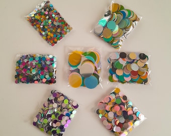 May include: Assortment of colorful iridescent sequins in clear plastic bags. The sequins are round and come in a variety of colors, including gold, silver, blue, green, red, and purple.