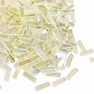 May include: A large collection of small, rectangular, translucent pale yellow plastic tags. Each tag features a smooth, flat surface with a single circular hole punched near one of the short ends, arranged in a scattered, overlapping pile.