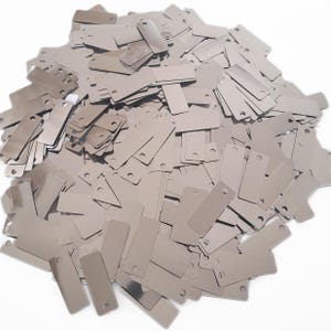 May include: A large pile of silver metal tags with two holes in each tag. The tags are rectangular and have a shiny, reflective surface.