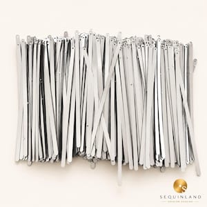 May include: A collection of long, thin, silver-colored metallic strips with rounded ends and small circular holes at the top. These slender, reflective pieces are arranged in a dense, overlapping pile, creating a uniform, shiny appearance.