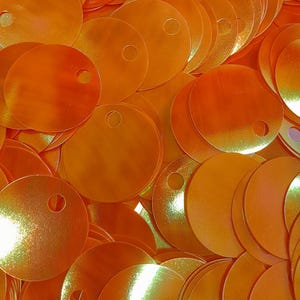 Pode incluir: Um monte de lantejoulas iridescentes laranja com um furo no centro de cada lantejoula.