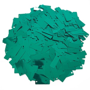 May include: A large pile of teal green metallic sequins in a rectangular shape. The sequins are scattered randomly and have a shiny finish.