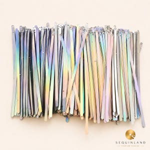 May include: A collection of long, thin, iridescent sequin strips featuring a metallic finish with shifting rainbow hues. Each individual strip is narrow and rectangular with a small hole at one end. The brand name Sequinland is printed in the corner.