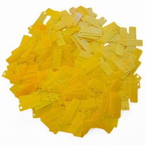 May include: A large pile of bright yellow rectangular sequins with two holes in each sequin.