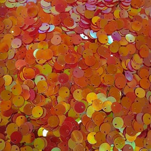 Könnte beinhalten: Ein großer Haufen von schimmernden orangefarbenen und roten runden Pailletten. Die Pailletten haben ein Loch in der Mitte zum Nähen.