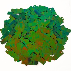 May include: A large pile of green, iridescent rectangular sequins with two holes in each. The sequins have a shimmery, holographic finish.
