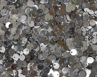 May include: A large pile of silver-colored metal round discs with a small hole in the center. The discs are all the same size and are arranged in a random pattern.