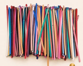May include: A collection of long, thin, rectangular sequins in a variety of vibrant colors including red, blue, green, gold, pink, and purple. Each individual sequin features a small circular hole at one end. The text Sequinland Premium Sequins appears.