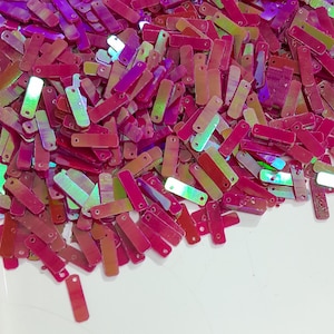May include: A pile of iridescent pink and green rectangular sequins with small holes at each end.