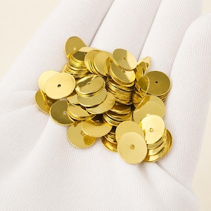 May include: A collection of small, circular, metallic gold sequins. Each individual disc features a single, centered hole for attachment. The sequins have a smooth, reflective, and polished surface, creating a bright, uniform appearance.