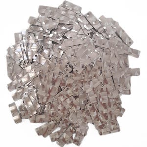 May include: A large pile of silver rectangular sequins with a slightly iridescent finish. The sequins have two small holes at the top.