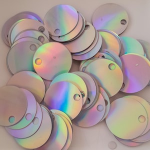 May include: A pile of iridescent round sequins with a hole in the centre. The sequins are a light silver colour with a rainbow sheen.