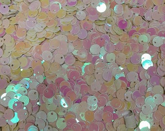 May include: A large pile of iridescent round sequins with a hole in the centre. The sequins are in shades of pink, yellow, and white.