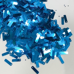 May include: A pile of turquoise blue rectangular sequins with small holes at each end.