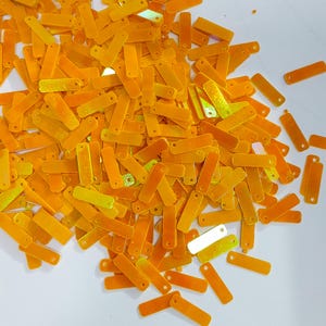 May include: A large pile of iridescent orange and yellow rectangular sequins with a hole at each end.